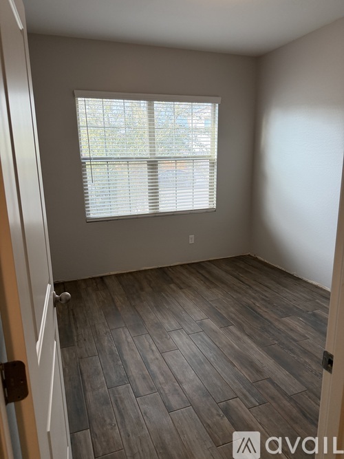 A room with a window covered by white blinds and wooden flooring.