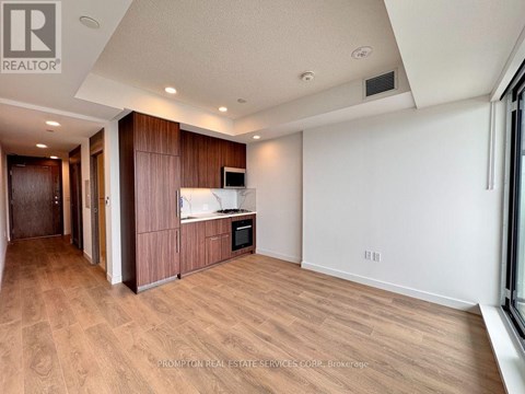 A spacious room with wooden flooring and a kitchen area with a microwave and oven.