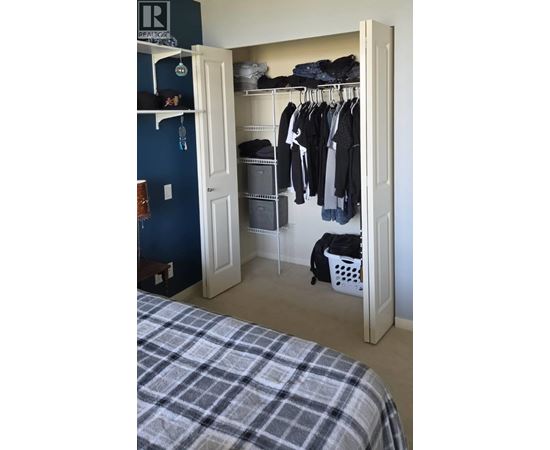 A bedroom with a bed and a closet with clothes hanging.