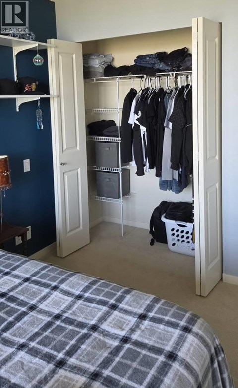 A bedroom with a bed and a closet with clothes hanging.