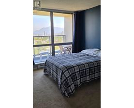 A bedroom with a bed, a chair, and a window overlooking a cityscape.
