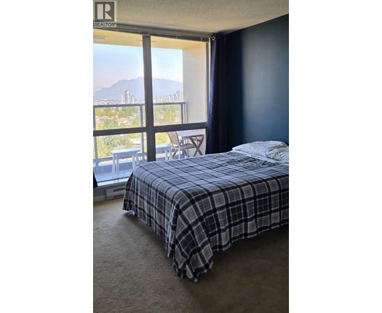 A bedroom with a bed, a chair, and a window overlooking a cityscape.