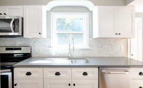 A kitchen with white cabinets and a grey countertop.