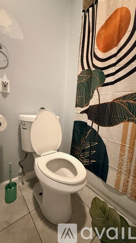 A toilet in a bathroom with a green plunger on the floor.