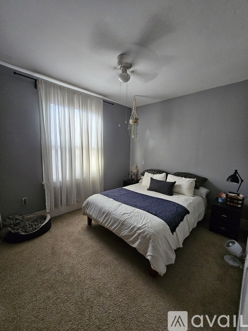 A bedroom with a bed, nightstand, and window with curtains.