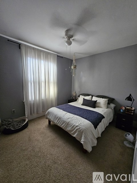A bedroom with a bed, nightstand, and window with curtains.