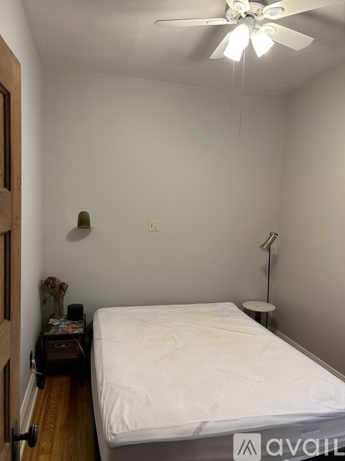 A bedroom with a bed, a ceiling fan, and a small table with a vase of flowers.