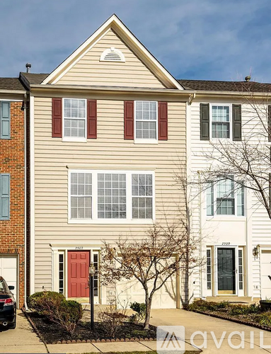 A two-story house with a red door and a tree in front.