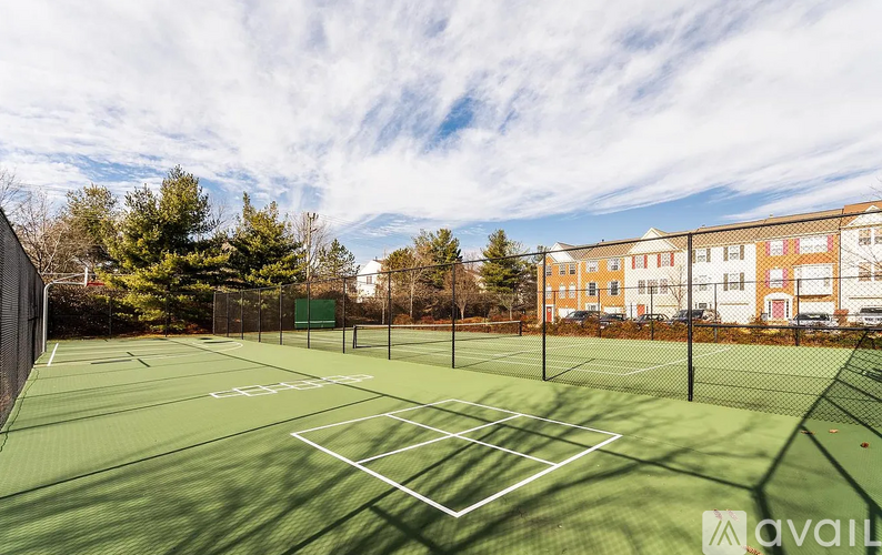 A tennis court with a green surface and white lines, surrounded by a fence and trees.