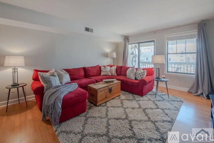 A red couch with a grey throw blanket sits in a living room with a grey rug and a wooden coffee table.