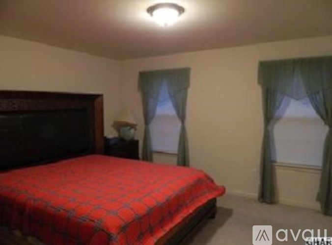 A bedroom with a red bedspread and a wooden headboard.