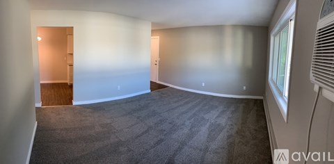 A spacious room with carpeted floor and a window on the right side.