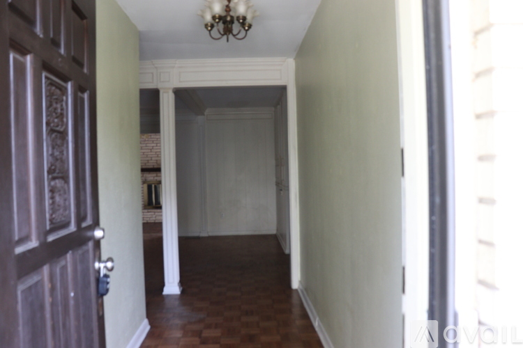 A hallway with a chandelier and a door on the left.