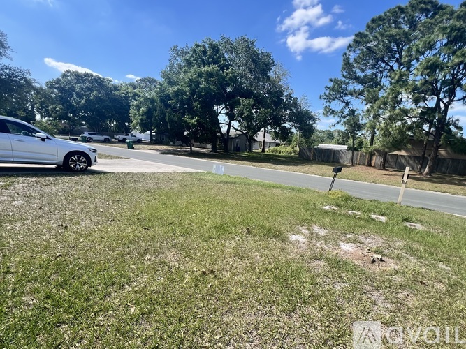 A white car is parked on the side of a road with trees in the background.