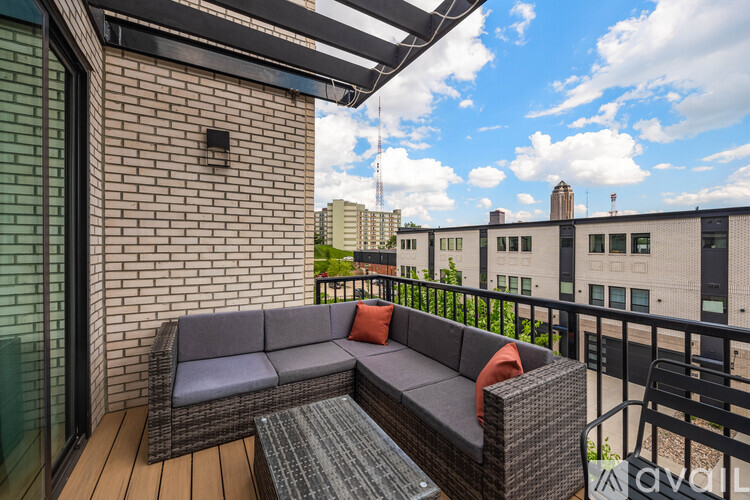 A patio with a grey couch and a glass table.