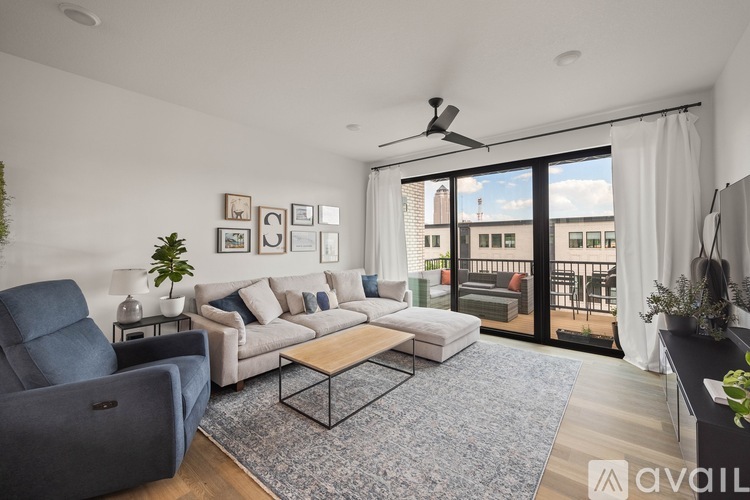 A living room with a grey sofa, a blue armchair, a wooden coffee table, and a large window with a view of the city.