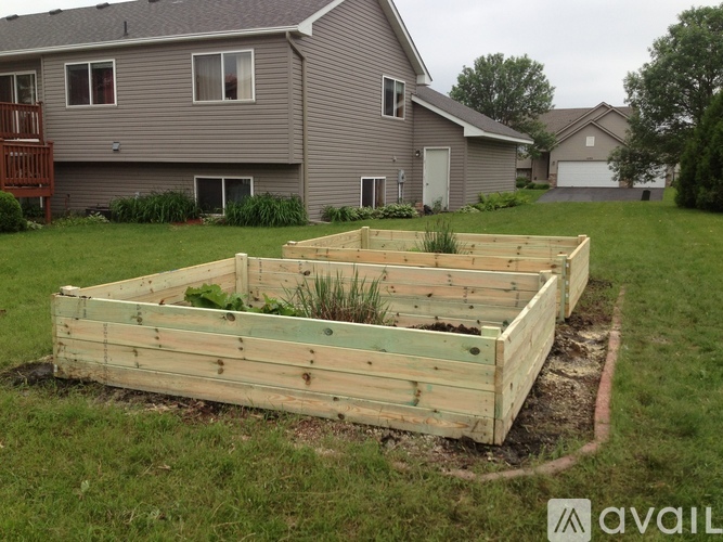 A wooden raised garden bed is in the foreground of a grassy area with a house in the background.