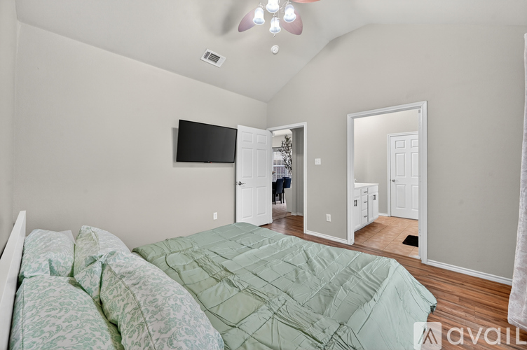 A bedroom with a bed covered in a green comforter and a flat screen TV mounted on the wall.