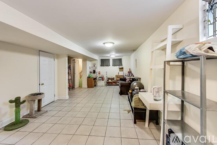 A spacious room with a white floor and walls, furnished with a desk, chairs, and a shelf.
