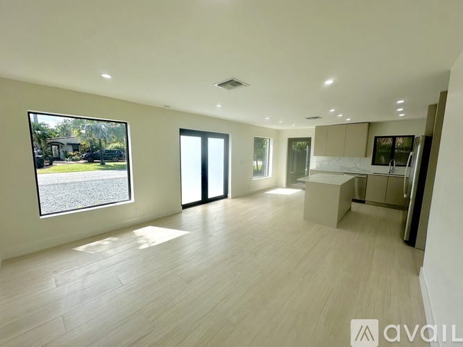 A spacious, well-lit room with wooden flooring and a large window overlooking a garden.