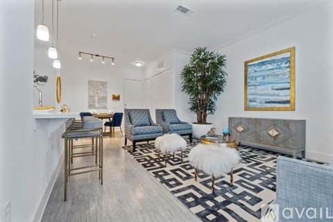 A living room with a black and white rug, a blue chair, and a painting on the wall.