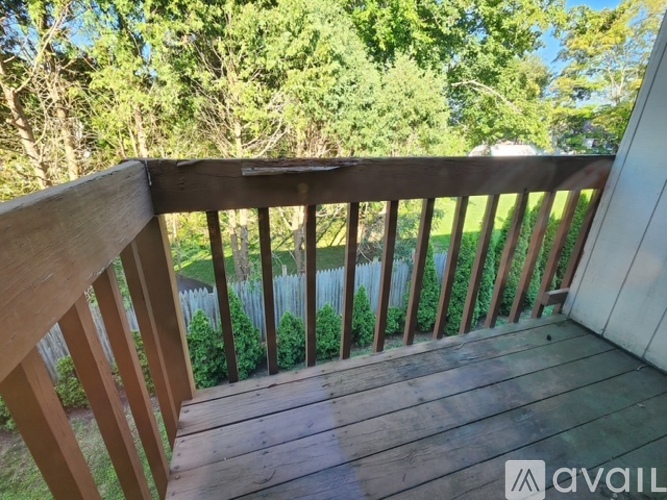 A wooden deck with a railing and a view of a fence and trees.