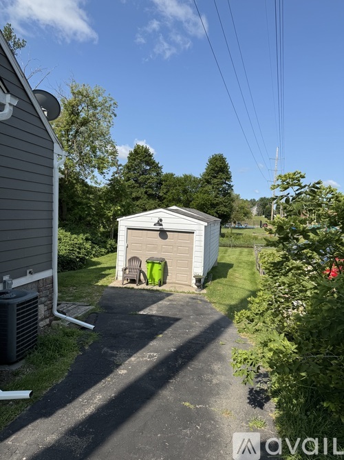 A small white shed sits in a grassy area next to a driveway.