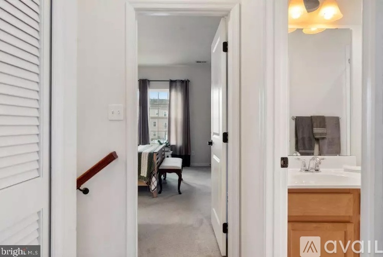 A bathroom with a sink, mirror, and a bedroom with a bed and chair in the background.
