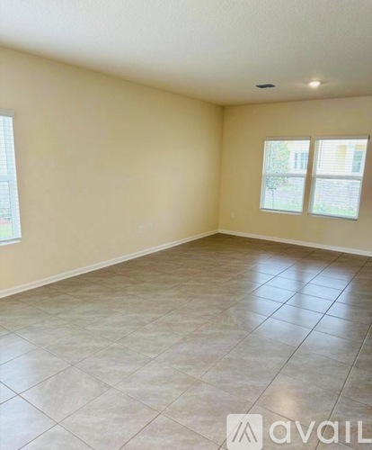 A spacious room with tile flooring and two windows.