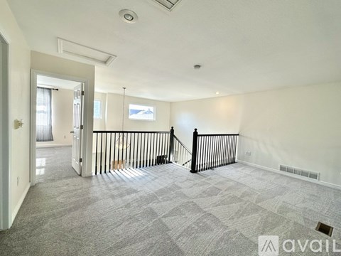 A spacious living room with a grey carpet and a black railing.