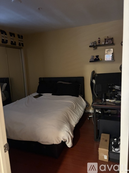 A bedroom with a bed, a desk with a computer, and a shelf with various items.