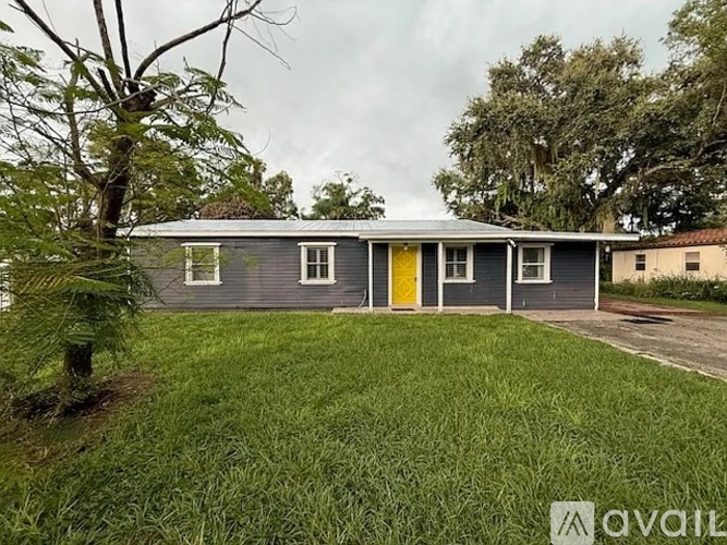 A grey house with a yellow door is surrounded by green grass.