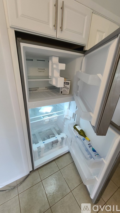 A white refrigerator with its door open and a bottle of wine on the door shelf.