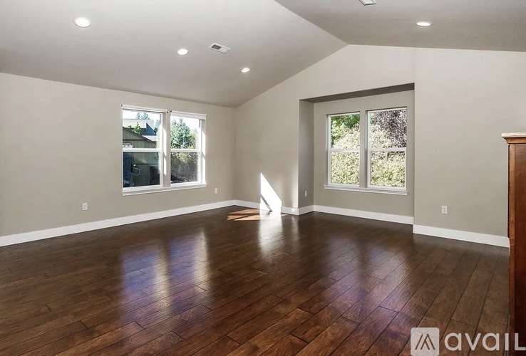 A spacious room with wooden floors and large windows.