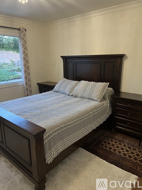 A bed with a wooden headboard and a striped comforter sits in a room with a window and a dresser.