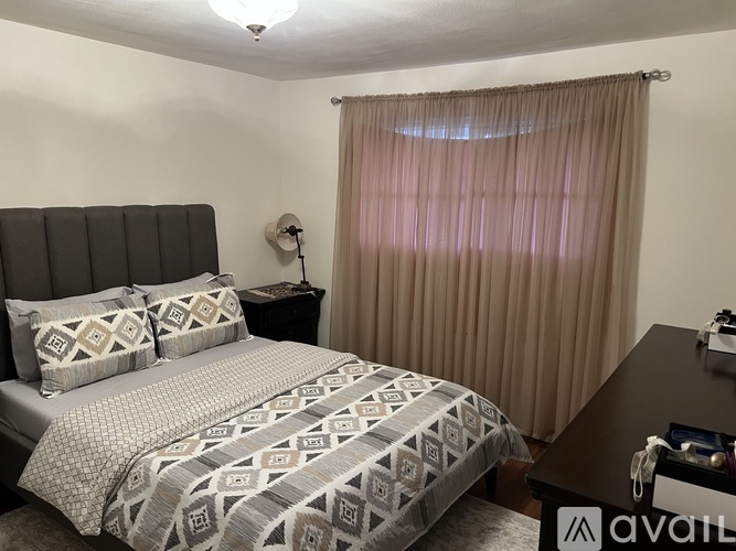 A bedroom with a large bed and a window with curtains.