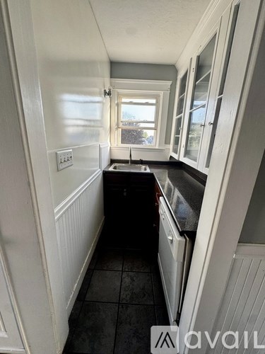 A narrow kitchen with white cabinets and a black countertop.