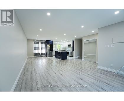 A spacious room with wooden flooring and a large window with curtains.