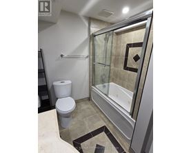 A bathroom with a toilet, a glass shower stall, and a tiled floor.