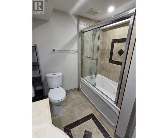 A bathroom with a toilet, a glass shower stall, and a tiled floor.