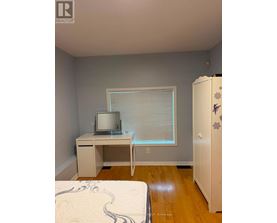 A bedroom with a bed, desk, and a refrigerator.