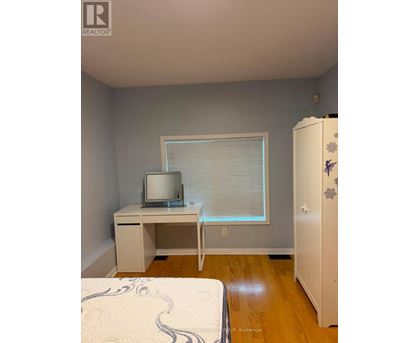 A bedroom with a bed, desk, and a refrigerator.