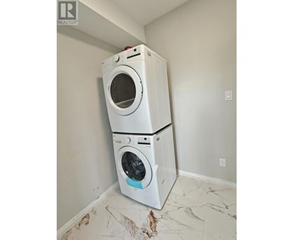 A white washing machine is stacked on top of another white washing machine in a room with white walls.
