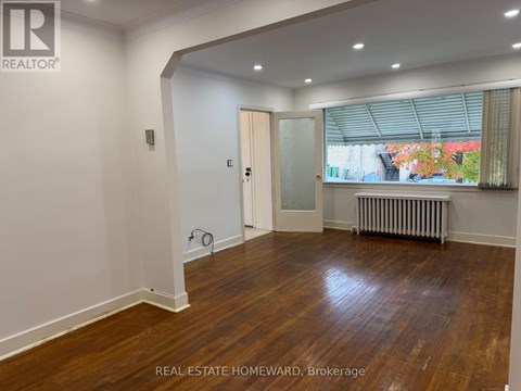 A room with wooden floors and white walls, with a door leading to a balcony.