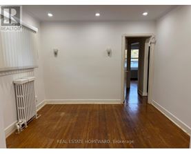 A room with wooden floors and white walls, with a doorway leading to another room.