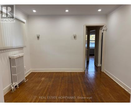 A room with wooden floors and white walls, with a doorway leading to another room.