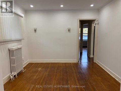 A room with wooden floors and white walls, with a doorway leading to another room.