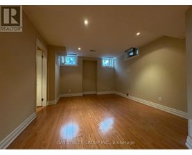 A spacious room with wooden flooring and two windows.