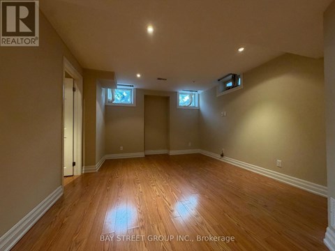 A spacious room with wooden flooring and two windows.