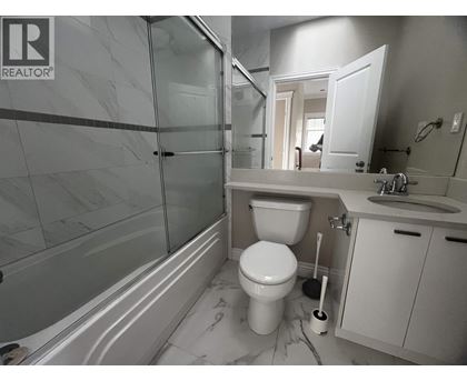 A white toilet sits in a bathroom with a marble floor and a glass shower.